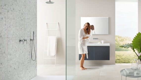Femme se séchant les cheveux avec une serviette dans une salle de bains avec douche ouverte et grands carreaux de style terrazzo