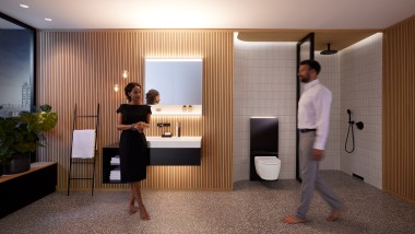 Homme et femme dans une salle de bains parfaitement éclairée avec les meubles de salle de bains et les céramiques sanitaires Geberit ONE (© Geberit)