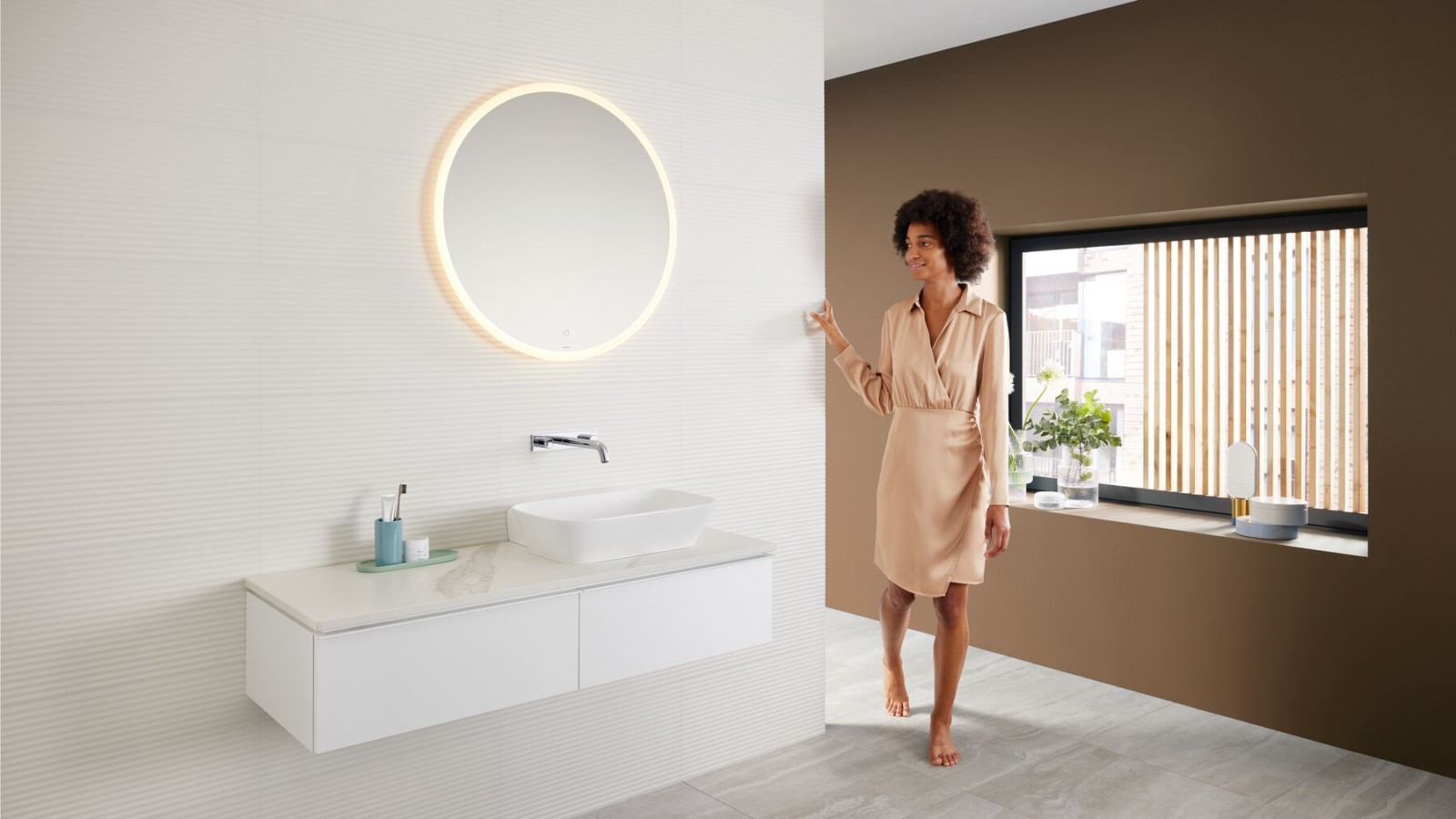 Une femme dans une salle de bains moderne avec une palette de couleurs brunes - la dernière tendance dans la salle de bains - et une combinaison de lavabos Mix & Match. Une femme dans une salle de bains moderne avec une palette de couleurs brunes - la dernière tendance dans la salle de bains - et une combinaison de lavabos Mix & Match.