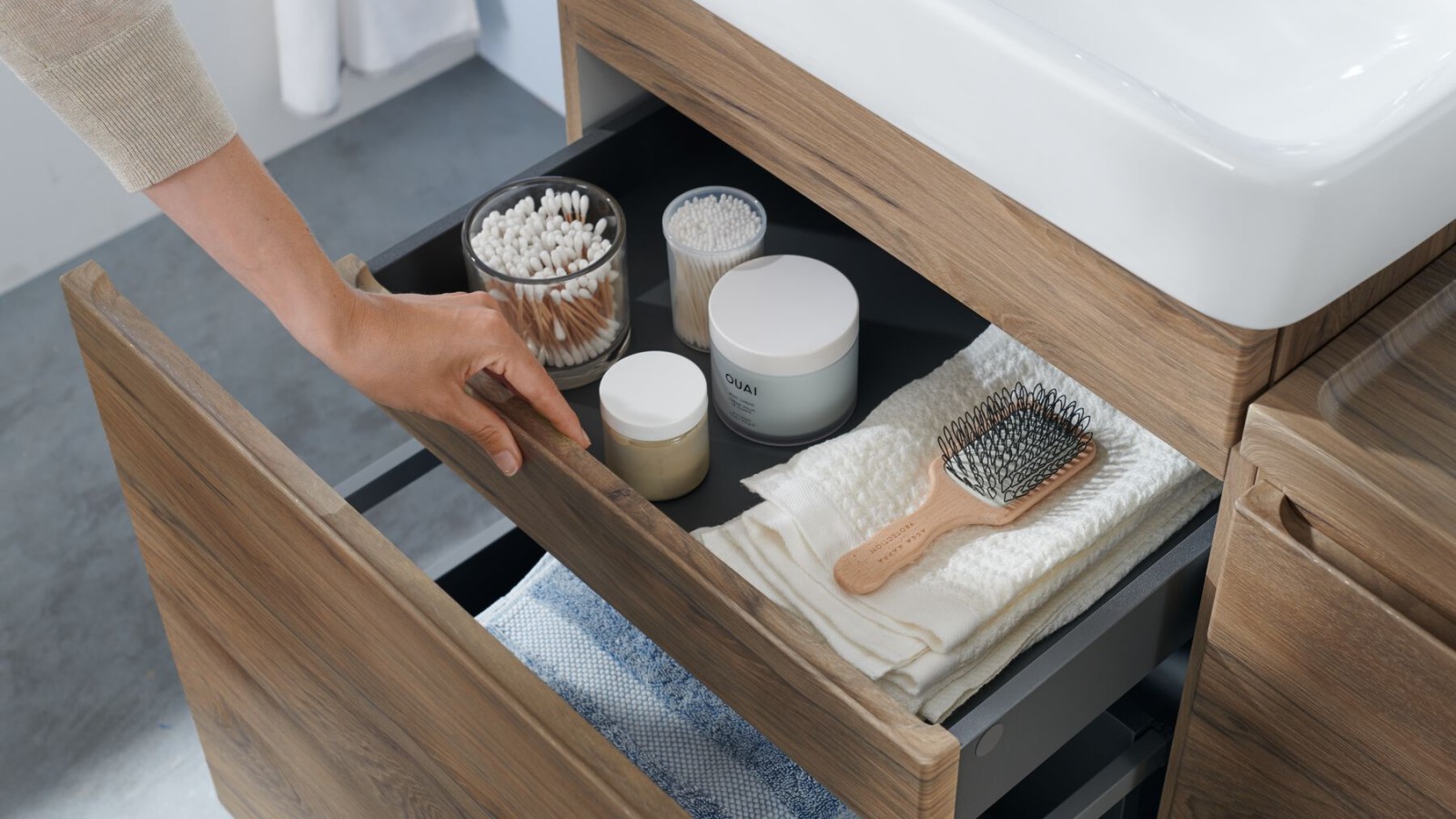 Une main ouvre l'un des tiroirs du sous-meuble Geberit Renova Plan au design bois naturel Une main ouvre l'un des tiroirs du sous-meuble Geberit Renova Plan au design bois naturel