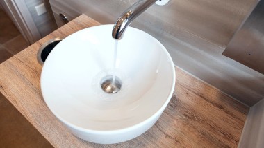 Wasser fliesst aus der Geberit Piave Wandarmatur in einen VariForm Aufsatzwaschtisch