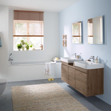 Salle de bains familiale au mur bleu clair avec meubles en noyer hickory, armoire à glace, plaque de déclenchement et céramiques de Geberit