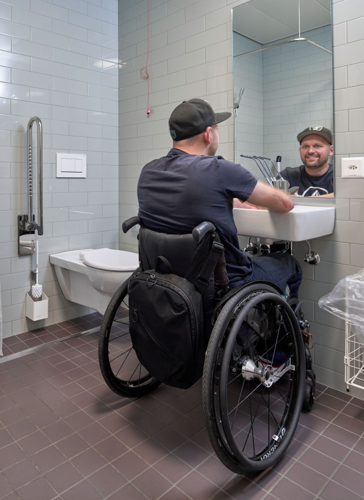 Peter Roos en fauteuil roulant au niveau de la zone de lavage dans une salle de bains adaptée aux PMR (© Ben Huggler)