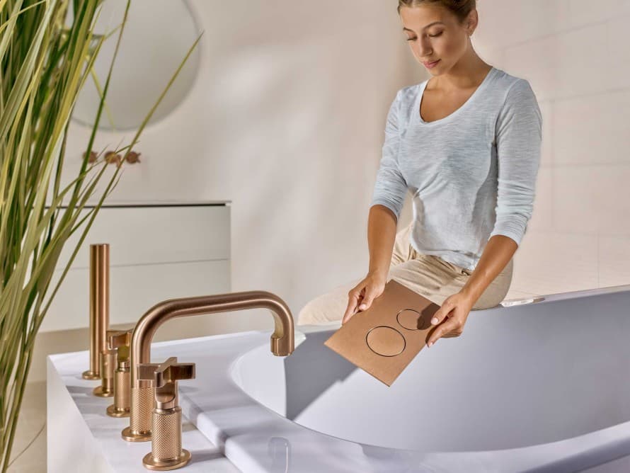 Femme dans une salle de bains équipée d’une plaque de déclenchement Sigma40 cuivre brossé assortie à la robinetterie Femme dans une salle de bains équipée d’une plaque de déclenchement Sigma40 cuivre brossé assortie à la robinetterie
