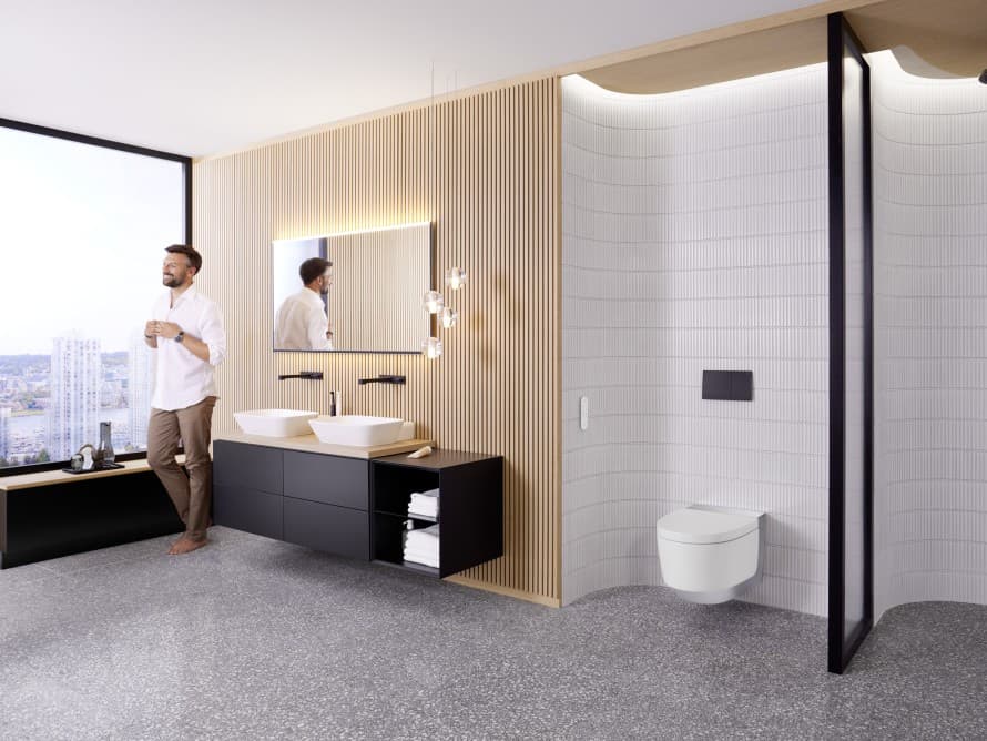 Mann in grossem Badezimmer mit dunklen Möbeln und Geberit AquaClean Dusch-WC Mann in grossem Badezimmer mit dunklen Möbeln und Geberit AquaClean Dusch-WC
